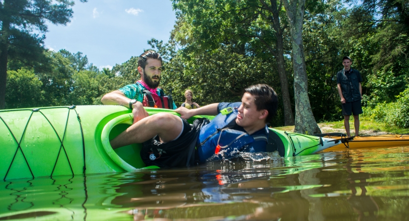During a safety exercise, a person flips their kayak over while an instructor braces it. 